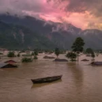 Submerged village in Northeast India during heavy monsoon floods, with rooftops above floodwater and hills behind